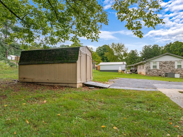 view of yard featuring central air condition unit, a storage shed, driveway, and an outbuilding