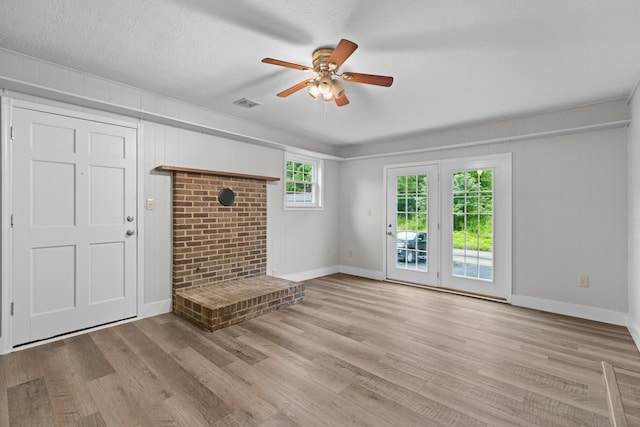 unfurnished living room with a textured ceiling, wood finished floors, visible vents, baseboards, and a ceiling fan