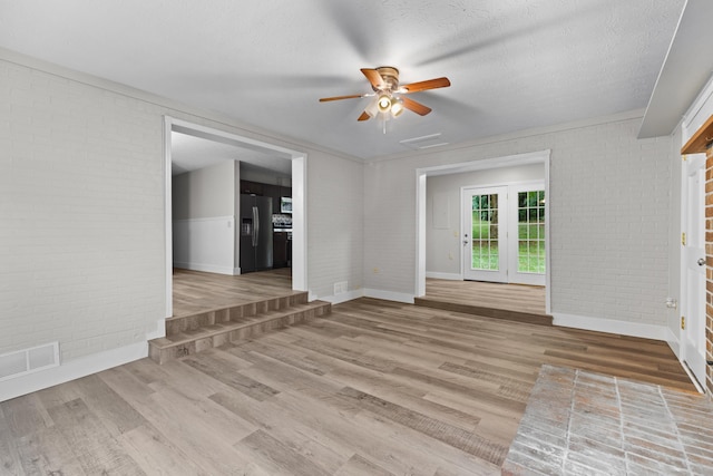 unfurnished living room with light wood-type flooring, visible vents, a textured ceiling, and brick wall