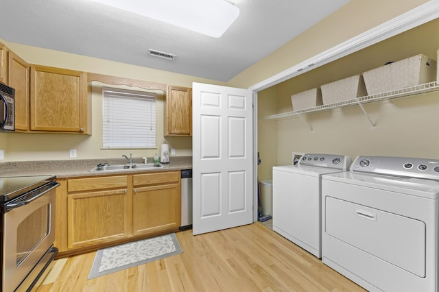 laundry area with washer and clothes dryer, light hardwood / wood-style flooring, and sink