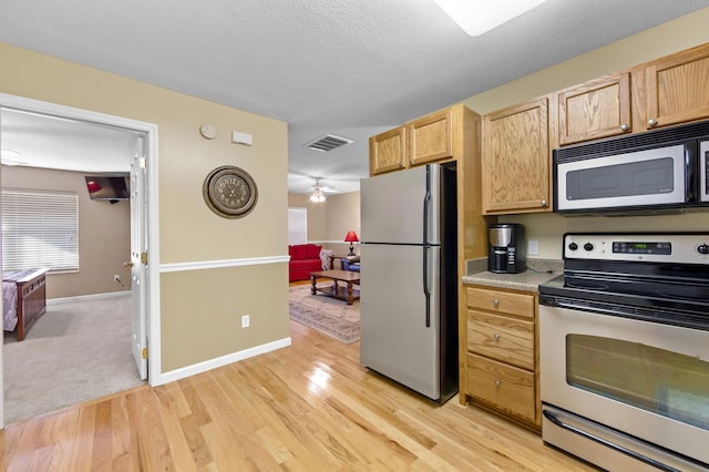 kitchen featuring ceiling fan, light hardwood / wood-style flooring, appliances with stainless steel finishes, light brown cabinets, and a textured ceiling