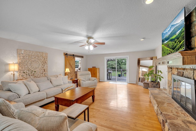 1216 Winding Dr, Sevierville, TN 37876 - living room with a barn door, a ceiling fan, a stone fireplace, a textured ceiling, and light wood finished floors