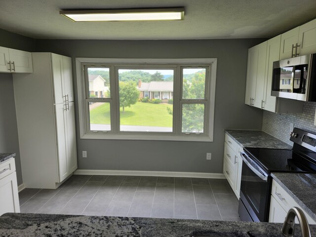 kitchen with backsplash, white cabinetry, stainless steel appliances, and dark stone counters