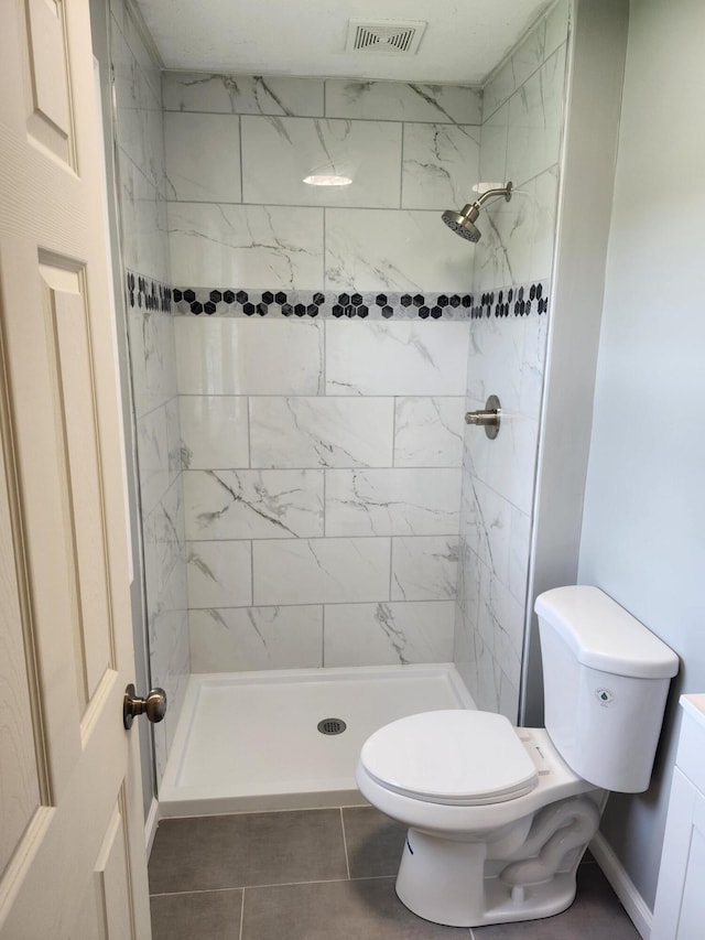 bathroom with tile patterned flooring, a tile shower, and toilet