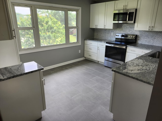 kitchen featuring tasteful backsplash, dark stone counters, stainless steel appliances, light tile patterned floors, and white cabinets