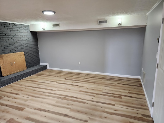 basement with a textured ceiling, light wood-type flooring, and crown molding