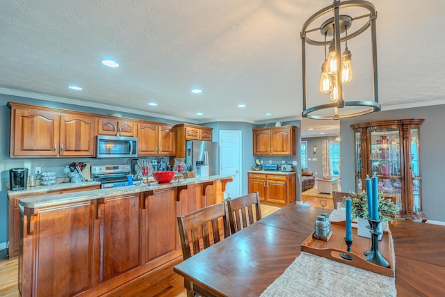 kitchen with appliances with stainless steel finishes, decorative light fixtures, crown molding, a textured ceiling, and light wood-type flooring