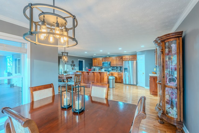 dining room featuring ornamental molding, a chandelier, a textured ceiling, and light wood-type flooring