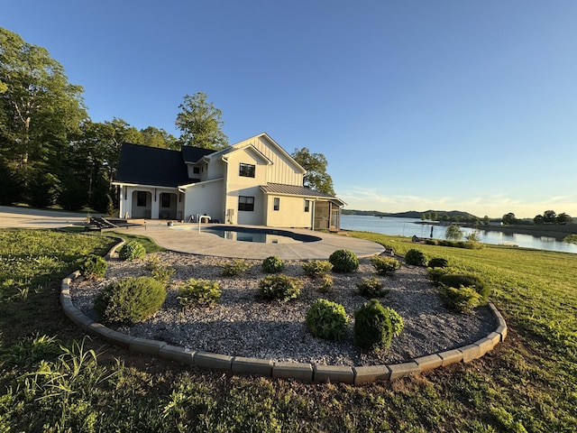 back of property featuring board and batten siding, a water view, a patio, and an outdoor pool