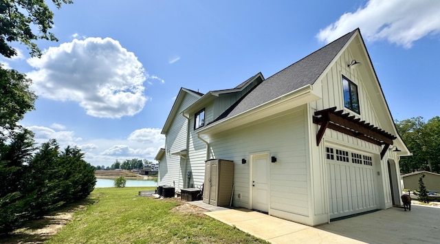 view of side of home with board and batten siding, a water view, central AC unit, a yard, and concrete driveway