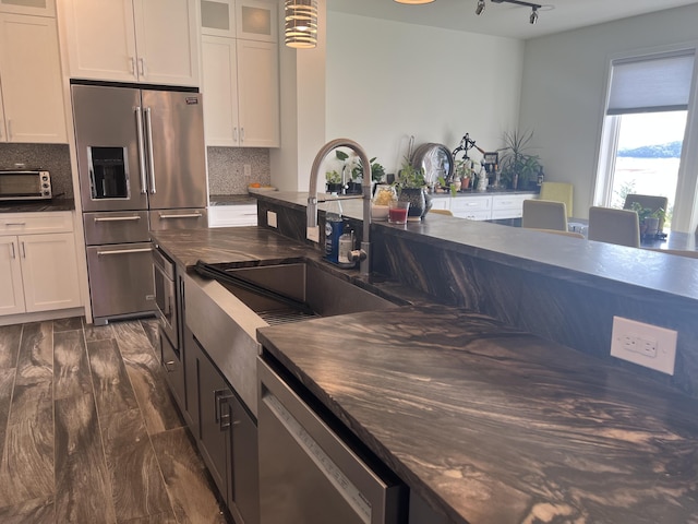 kitchen featuring stainless steel appliances, dark countertops, white cabinetry, glass insert cabinets, and tasteful backsplash