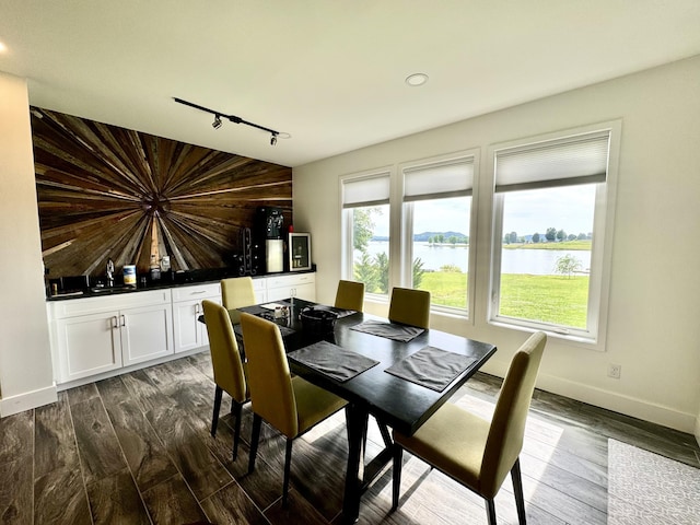 dining room with rail lighting, a water view, dark wood-style floors, baseboards, and recessed lighting