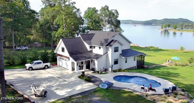 rear view of property featuring a water view, board and batten siding, concrete driveway, a lawn, and a shingled roof