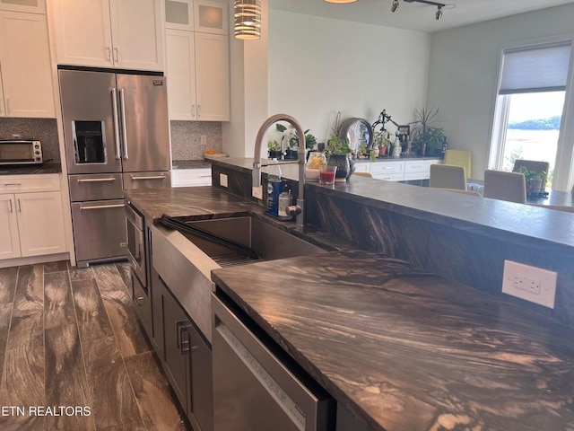 kitchen featuring stainless steel appliances, dark countertops, a sink, and white cabinetry