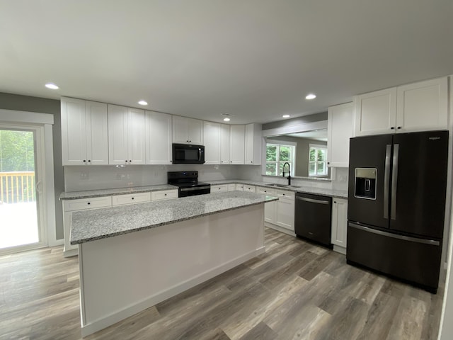 kitchen featuring sink, white cabinetry, light stone counters, wood-type flooring, and black appliances