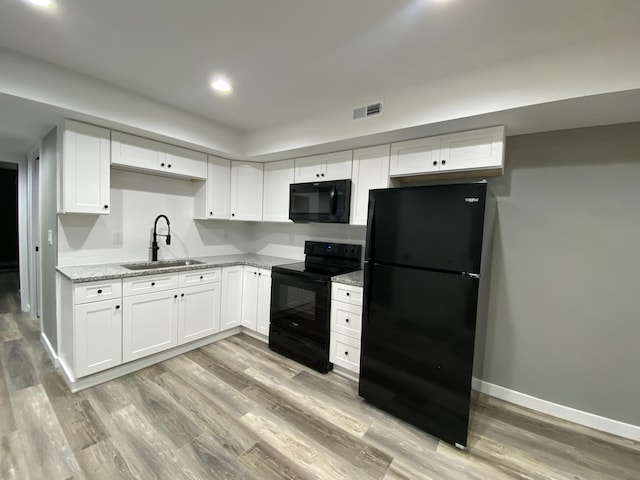 kitchen with light stone countertops, white cabinetry, sink, light hardwood / wood-style floors, and black appliances