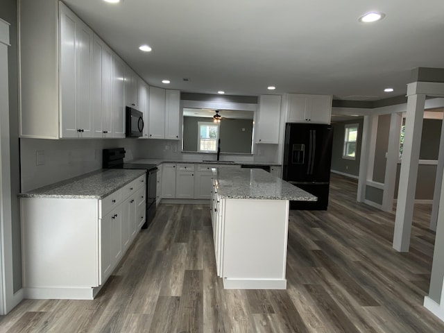 kitchen with black appliances, sink, a kitchen island, light stone counters, and white cabinetry