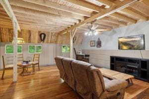 living area with a fireplace, a ceiling fan, beamed ceiling, and wood finished floors