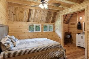 bedroom featuring lofted ceiling with beams, wooden walls, and wood finished floors