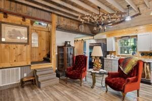 living area featuring a barn door, a notable chandelier, wood finished floors, visible vents, and beamed ceiling