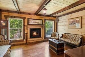 sitting room with wood walls, beamed ceiling, and wood finished floors