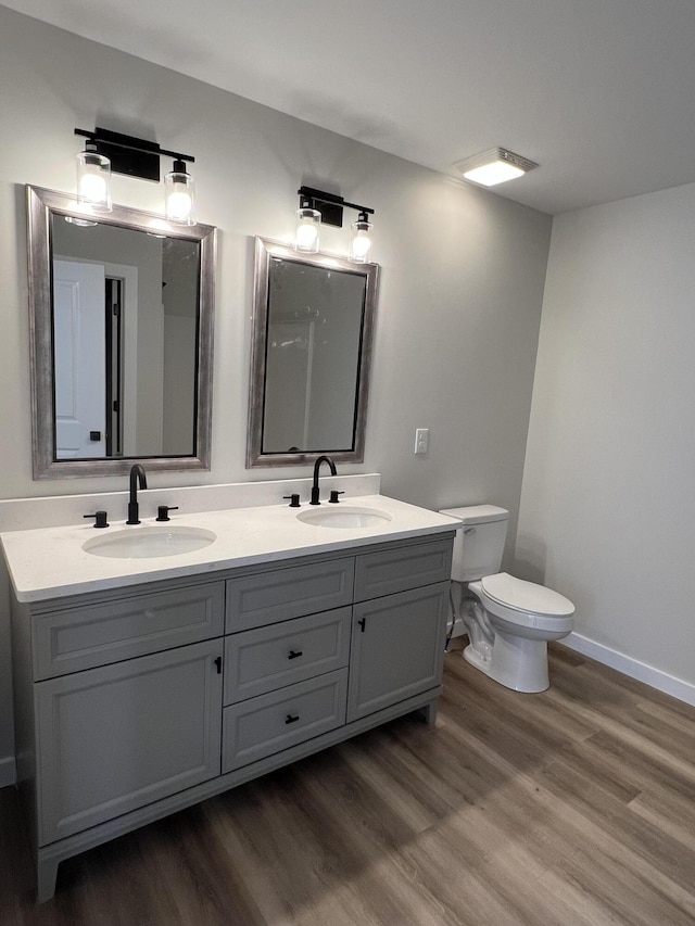 bathroom featuring double vanity, wood finished floors, a sink, and toilet