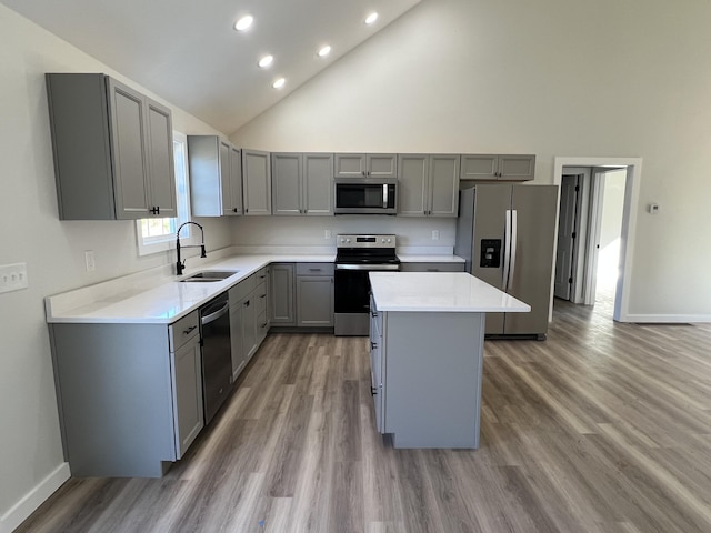 kitchen with a sink, a kitchen island, light countertops, appliances with stainless steel finishes, and gray cabinets