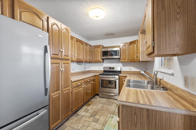 kitchen with wooden counters, appliances with stainless steel finishes, sink, and a textured ceiling