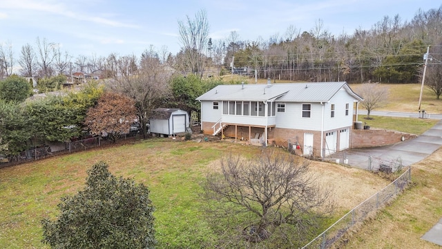 rear view of house featuring a garage, a sunroom, a storage unit, and a lawn