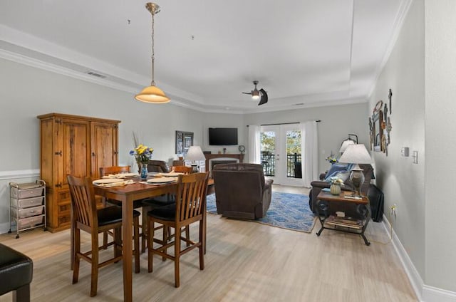 dining area featuring baseboards, a raised ceiling, crown molding, french doors, and light wood-style floors