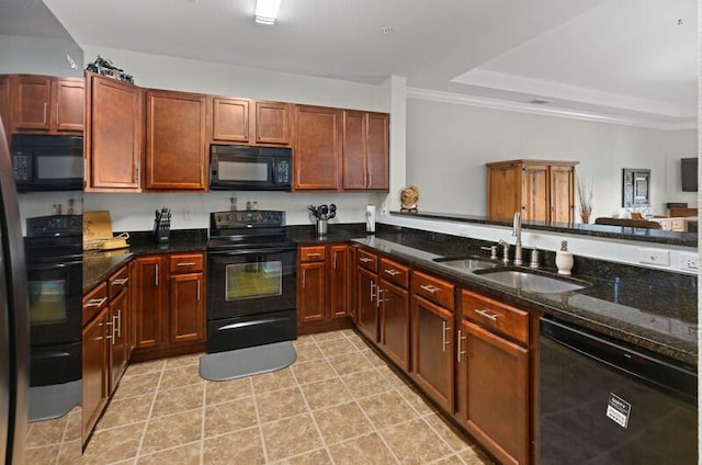 kitchen featuring a peninsula, a sink, black appliances, a tray ceiling, and dark stone countertops