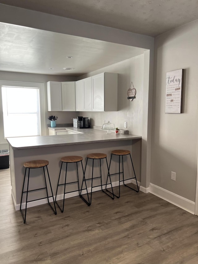 kitchen featuring light wood-type flooring, white cabinets, a kitchen bar, and kitchen peninsula