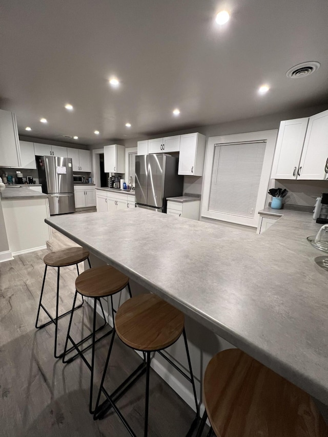 kitchen featuring a breakfast bar, white cabinets, and stainless steel refrigerator