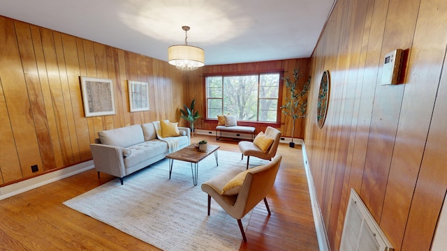 living room featuring a notable chandelier, wood walls, and light wood-type flooring