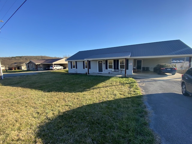 ranch-style home featuring metal roof, a carport, a front lawn, and driveway