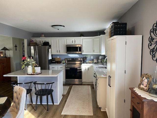 kitchen with dark wood finished floors, stainless steel appliances, light countertops, white cabinetry, and a sink