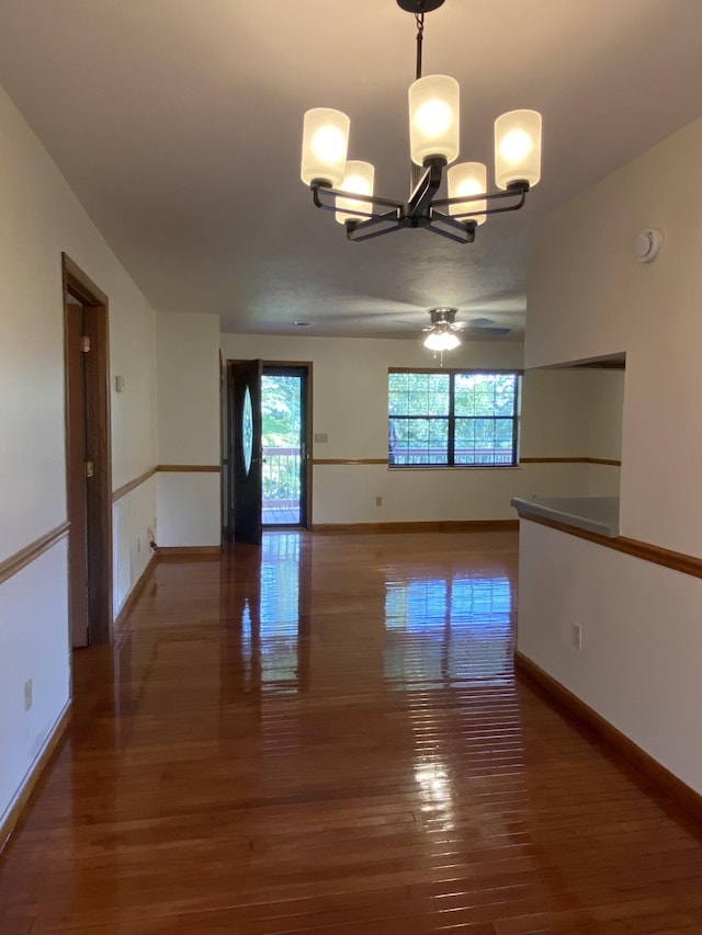 spare room featuring ceiling fan with notable chandelier and dark wood-type flooring