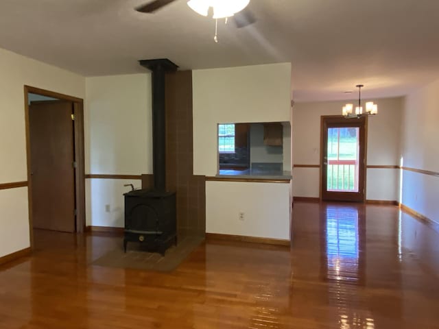 unfurnished living room featuring ceiling fan with notable chandelier, wood-type flooring, and a wood stove