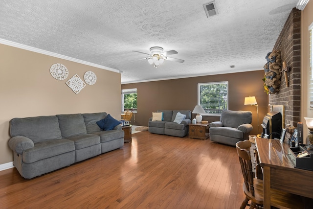 living room with ceiling fan, visible vents, crown molding, and wood finished floors