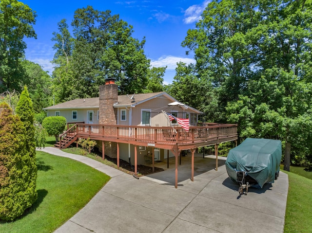 rear view of house with driveway, a chimney, a lawn, and a wooden deck