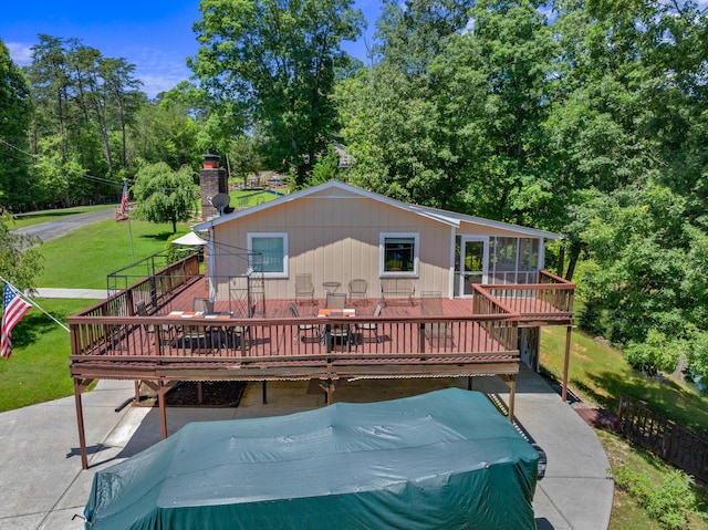 back of house with a sunroom, a chimney, a deck, and a lawn