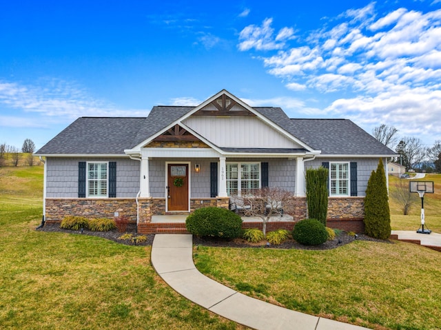 craftsman-style home with stone siding, a shingled roof, and a front yard