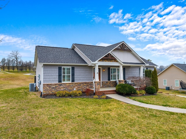 craftsman-style home with a porch, central AC, stone siding, roof with shingles, and a front yard