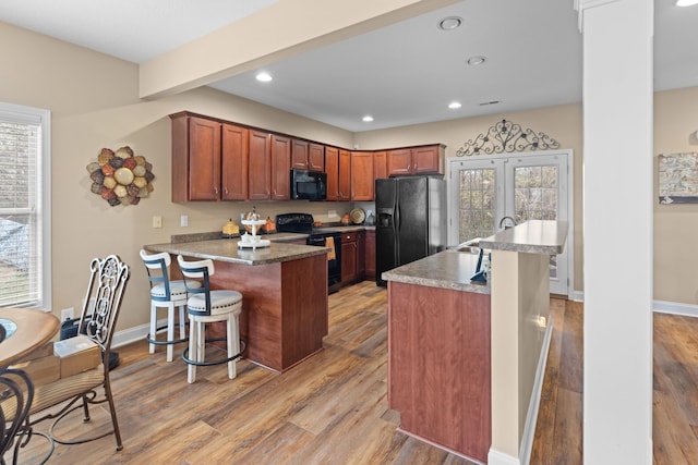 kitchen featuring sink, light hardwood / wood-style flooring, a kitchen bar, a kitchen island with sink, and black appliances