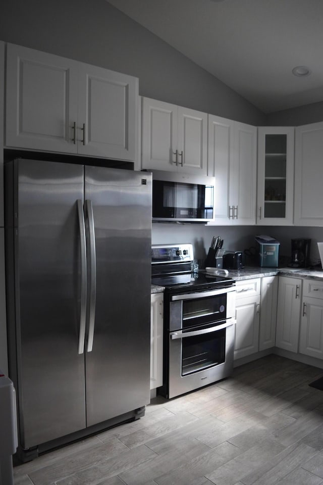 kitchen featuring stainless steel appliances, white cabinetry, vaulted ceiling, and light wood-type flooring