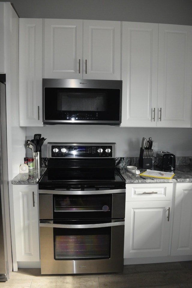 kitchen with dark stone countertops, appliances with stainless steel finishes, and white cabinets