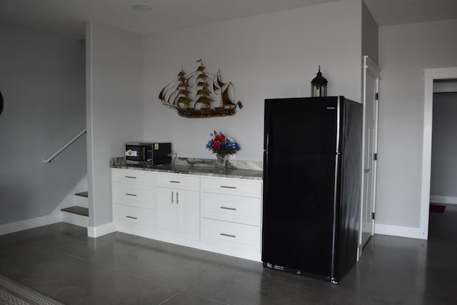 kitchen with white cabinets, stone counters, and black fridge