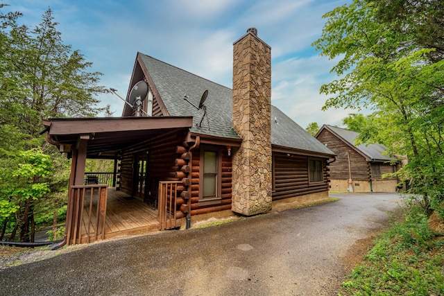 log home with a chimney, log exterior, a shingled roof, a wooden deck, and aphalt driveway