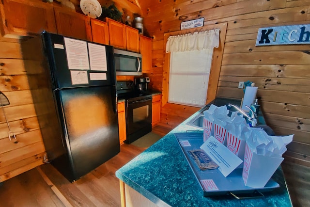 kitchen with wooden walls, light hardwood / wood-style flooring, and black appliances