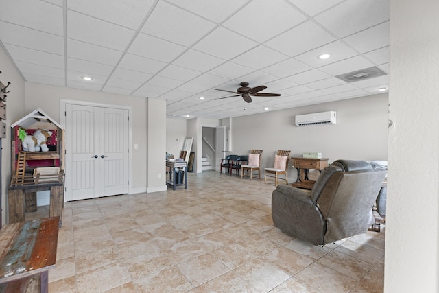 living room with a wall mounted air conditioner, ceiling fan, and a paneled ceiling